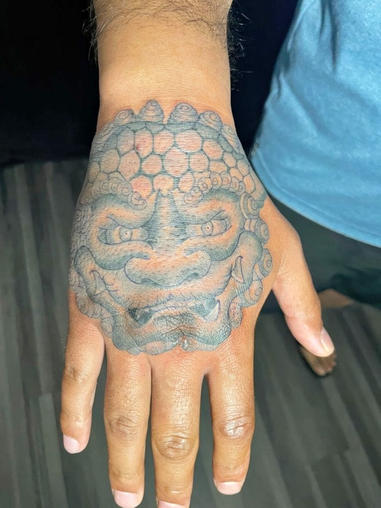 Tattoo of a fierce, smiling lions face on the back of the hand.