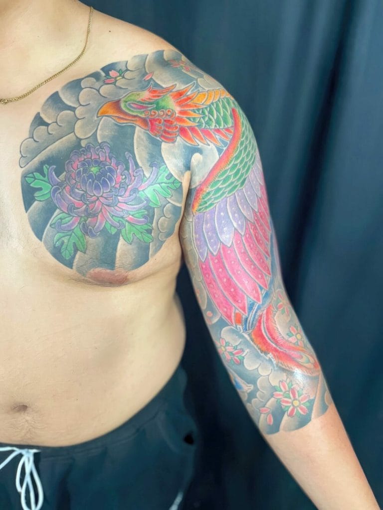 Colorful dragon and floral tattoo covering shoulder and arm against a dark background.