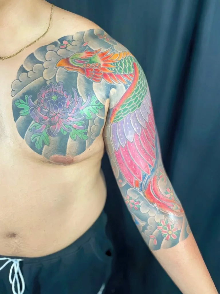 Colorful dragon and floral tattoo covering shoulder and arm against a dark background.
