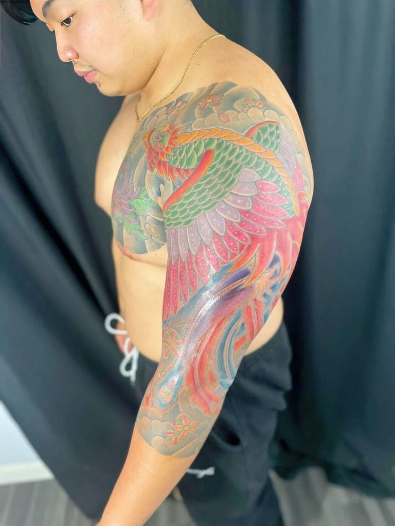 Colorful dragon and floral tattoo covering the shoulder and arm of a shirtless man.