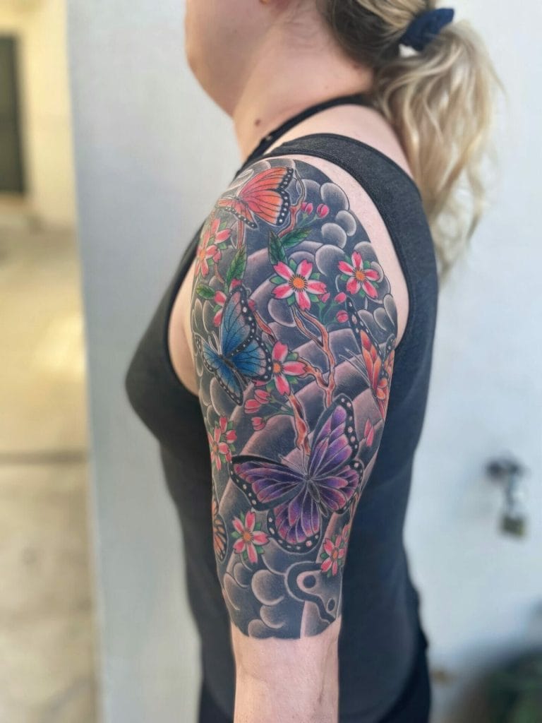 Colorful butterfly and cherry blossom tattoo on womans upper arm and shoulder.