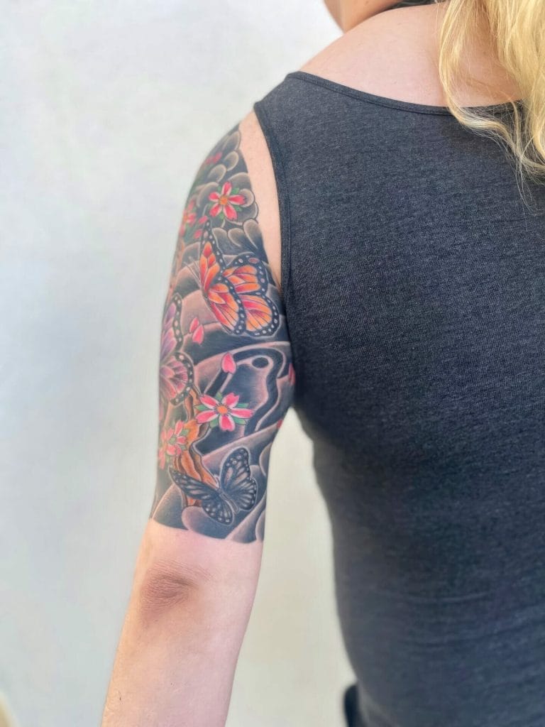 Colorful butterfly and flower tattoo on persons upper arm and shoulder.