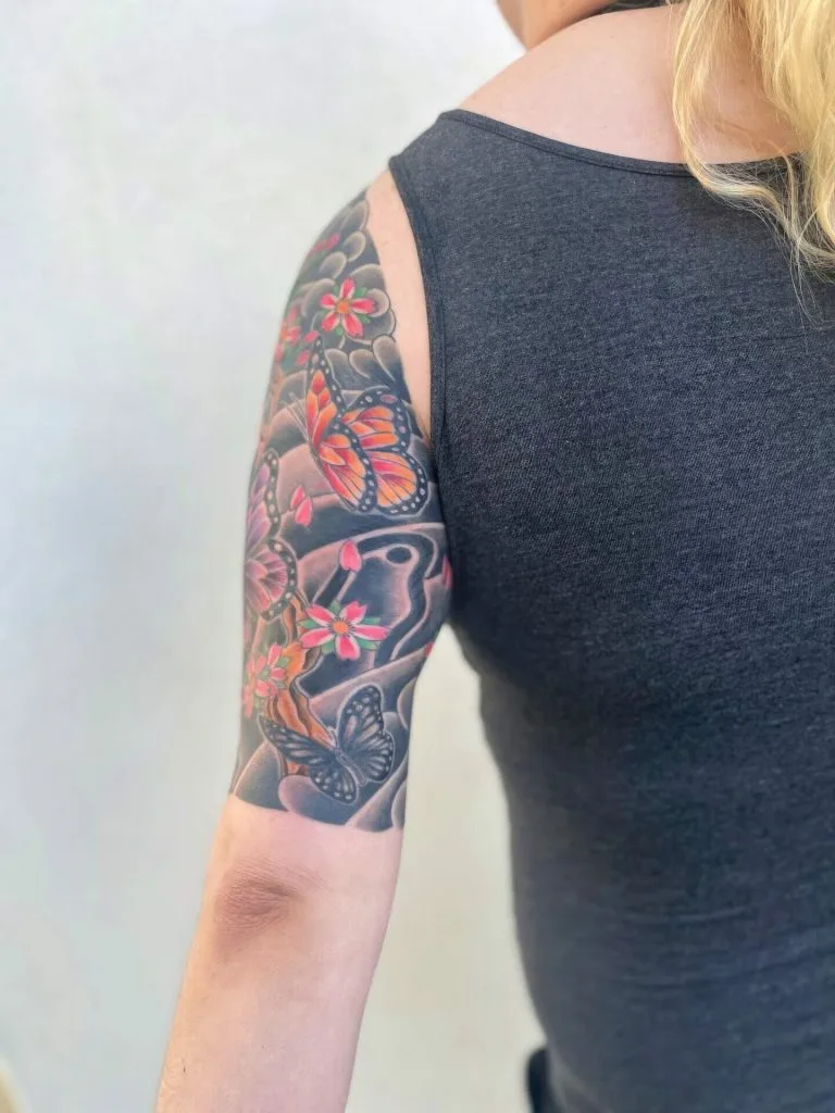 Colorful butterfly and flower tattoo on persons upper arm and shoulder.