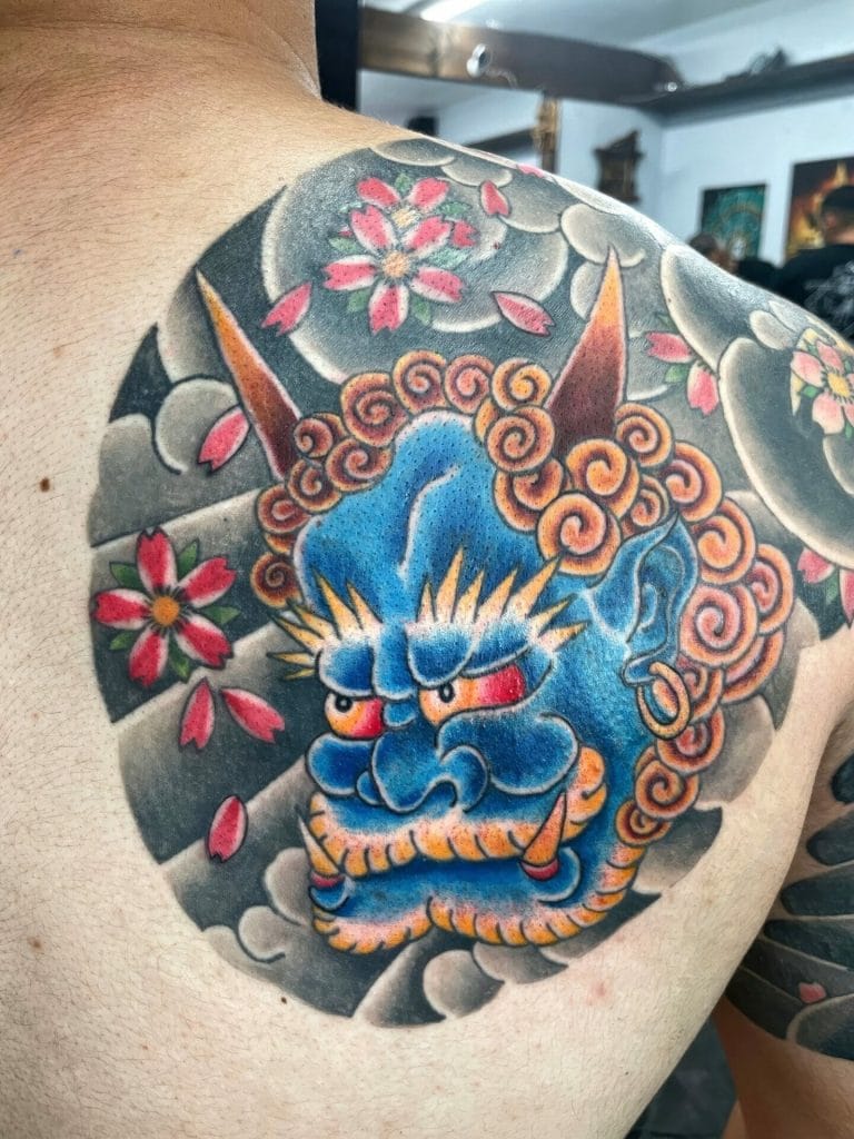 Colorful dragon tattoo with pink cherry blossoms and gray clouds on persons shoulder.