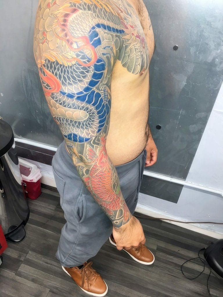 Colorful dragon tattoo covering the persons shoulder, arm, and chest.