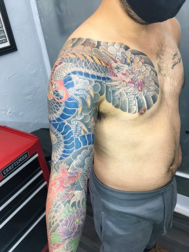 Colorful Japanese-style dragon tattoo covering the shoulder and arm, with clouds and flowers.