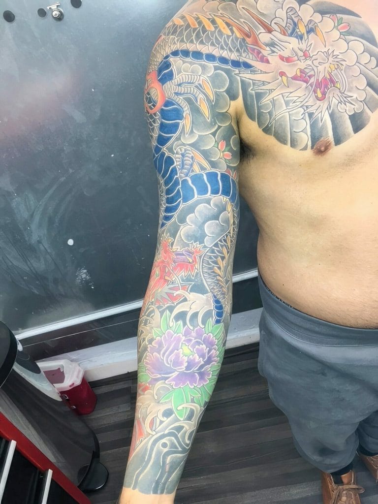 Colorful dragon and floral tattoo covering the persons arm and shoulder.