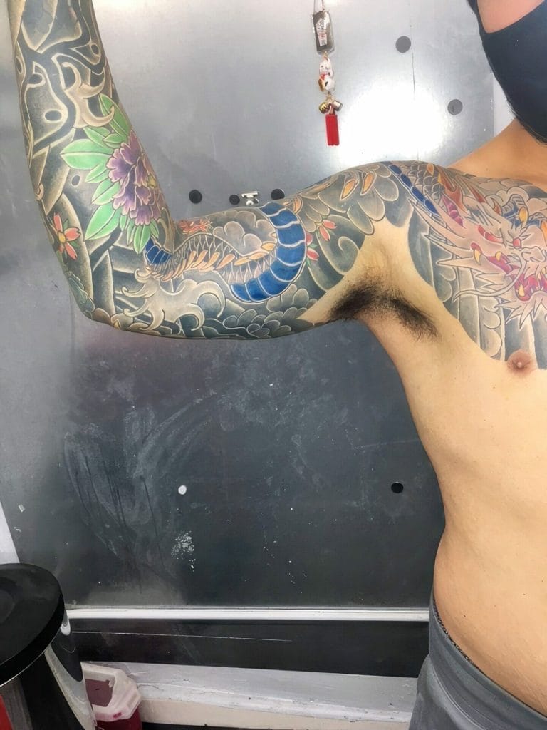 Colorful tattoo sleeve with a dragon, flowers, and clouds on a persons arm.
