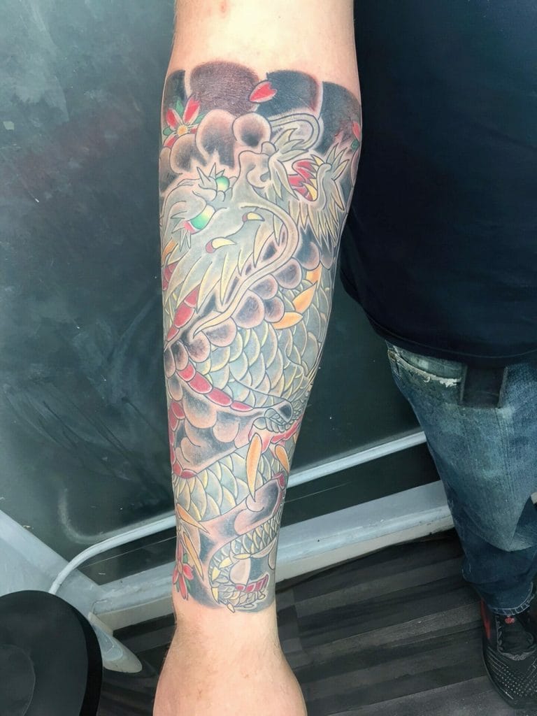 Detailed tattoo of a dragon with scales, claws, and flowing mane covering the forearm.