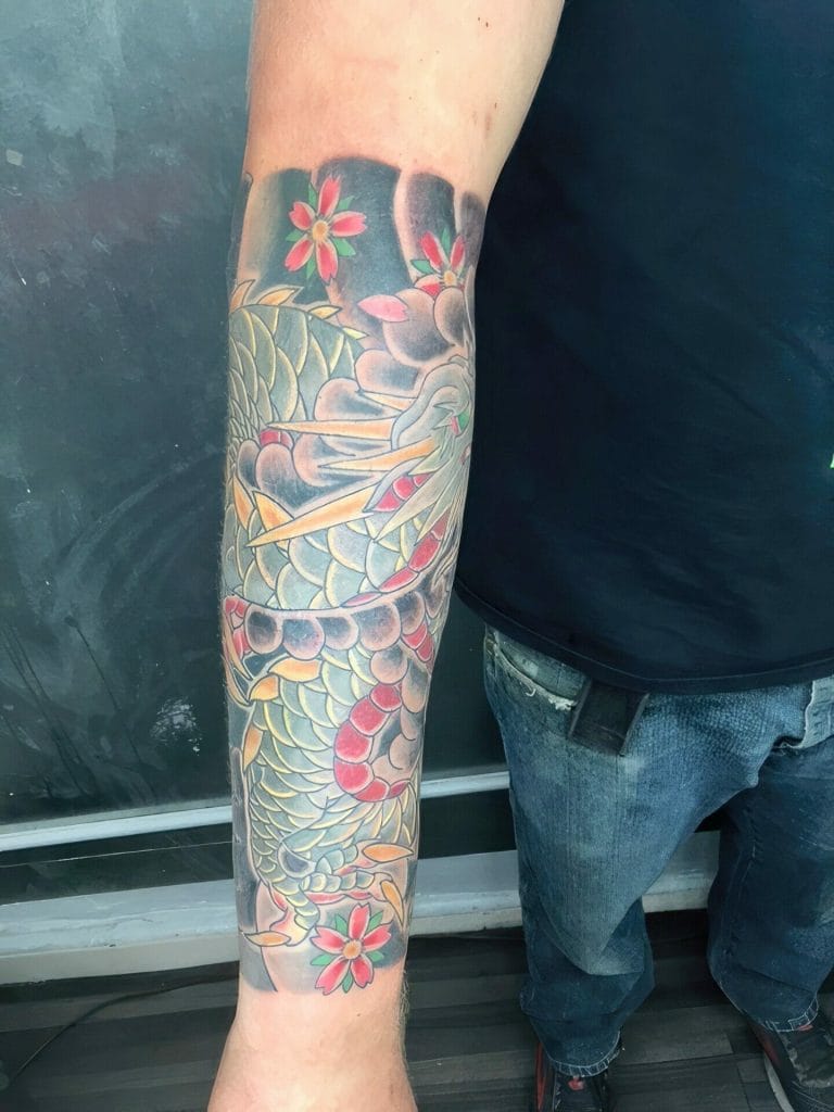 Colorful dragon tattoo with pink flowers on persons forearm.