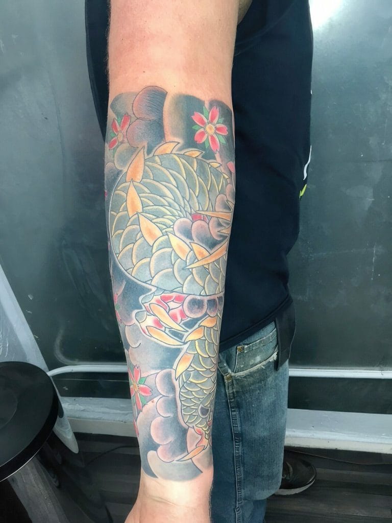 Colorful koi fish tattoo with pink flowers and clouds on persons forearm.