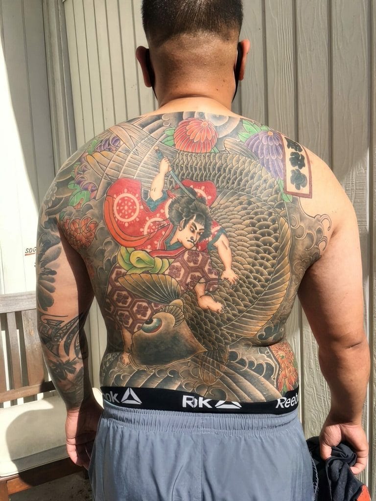 Back view of a person with a large, colorful Japanese-style dragon and warrior tattoo covering the back and right arm.