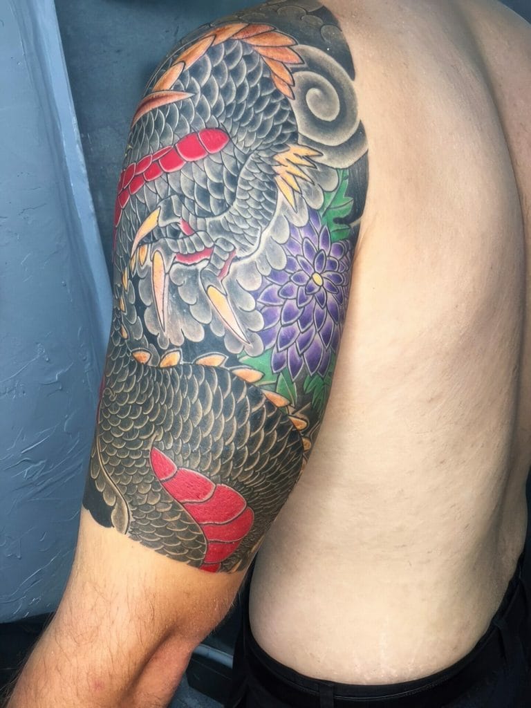 Colorful dragon tattoo with scales, claws, and purple flowers on persons upper arm.