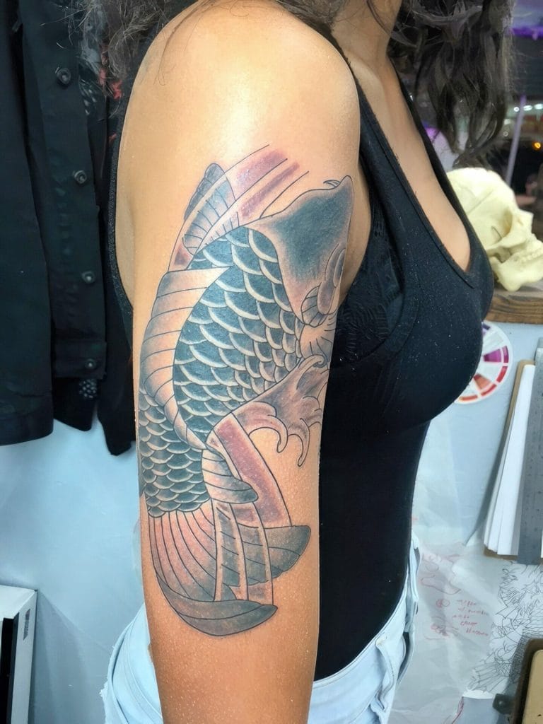 Detailed black and gray koi fish tattoo on upper arm with scales and flowing fins.
