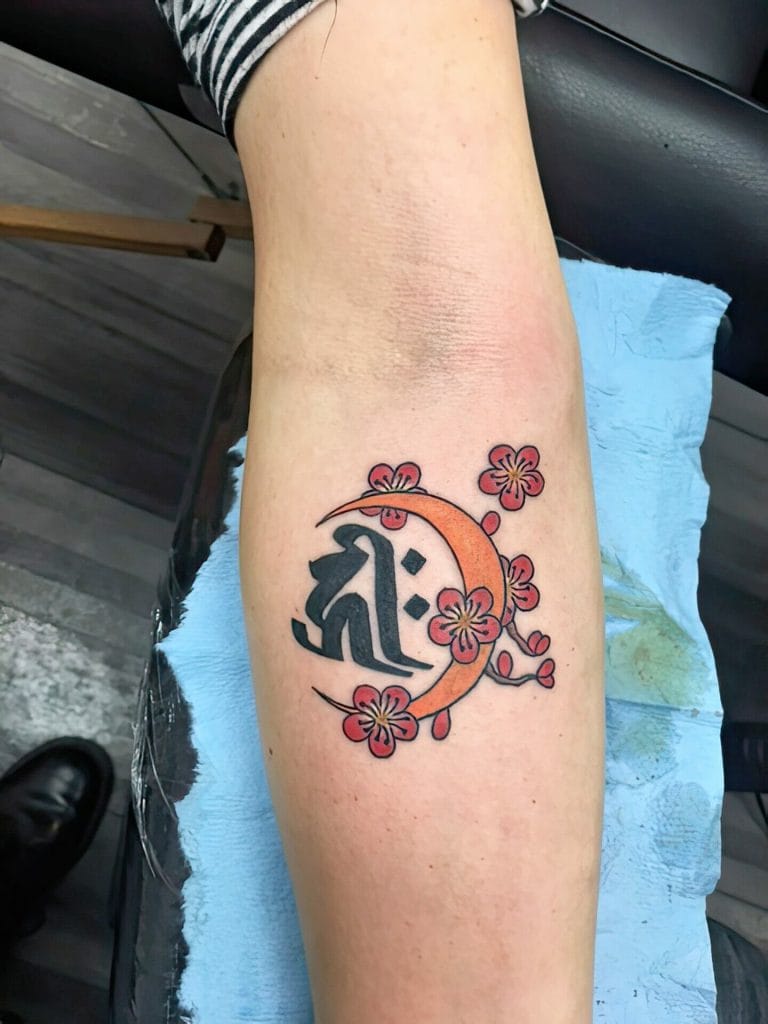 Black Chinese character with orange crescent moon and pink cherry blossoms around it.