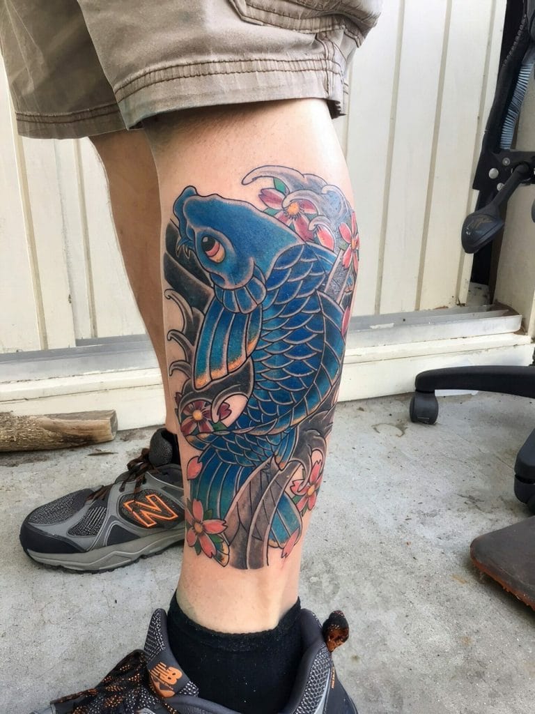 Blue koi fish with pink flowers and green leaves on persons calf.