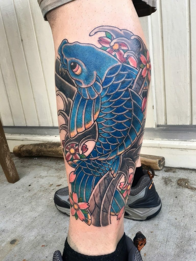 Blue koi fish swimming among pink cherry blossoms on persons leg tattoo.