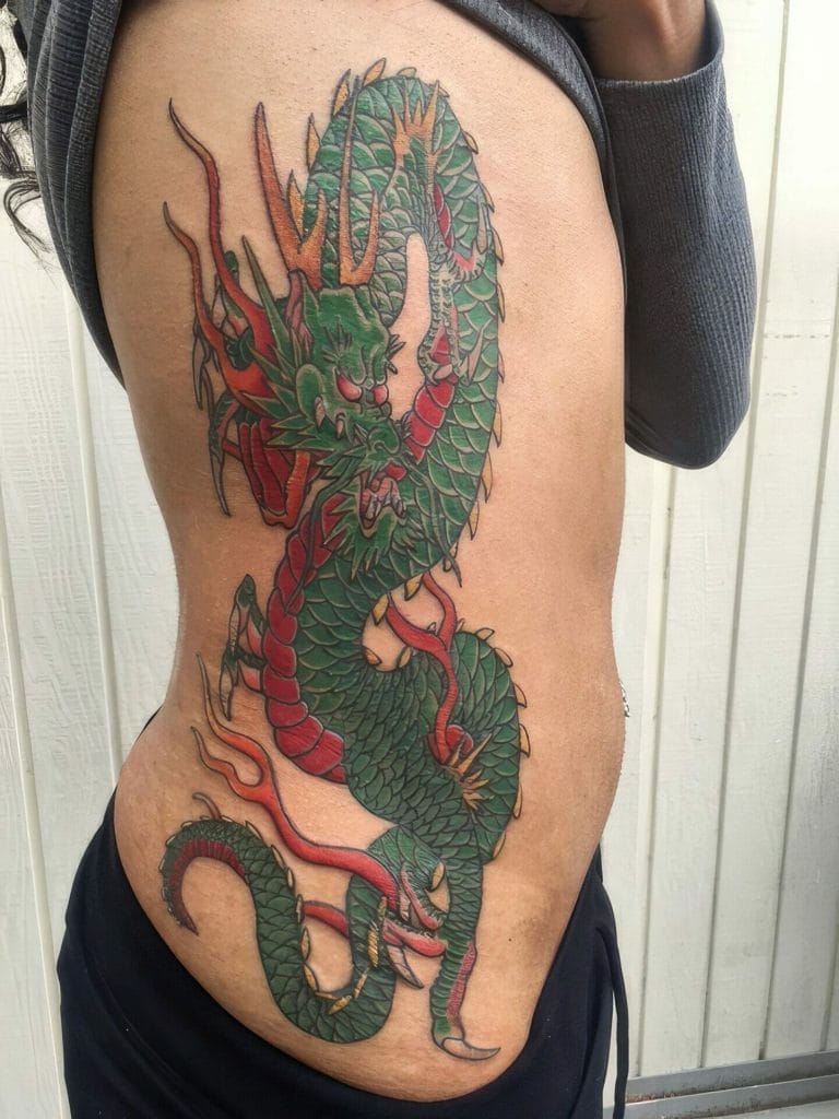 Colorful dragon tattoo with green scales, red accents, and orange horns on persons side.