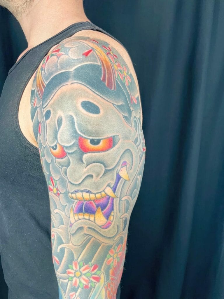 Colorful traditional Japanese Hannya mask tattoo with flowers on persons upper arm.