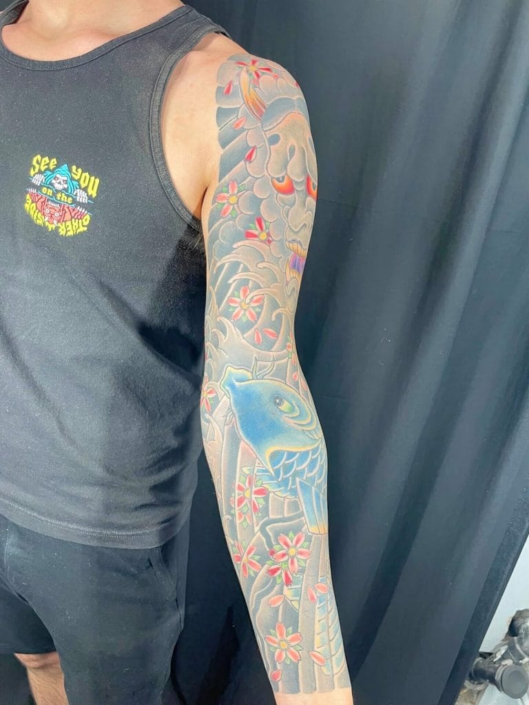 Colorful Japanese-style sleeve tattoo with a blue bird, cherry blossoms, and clouds.