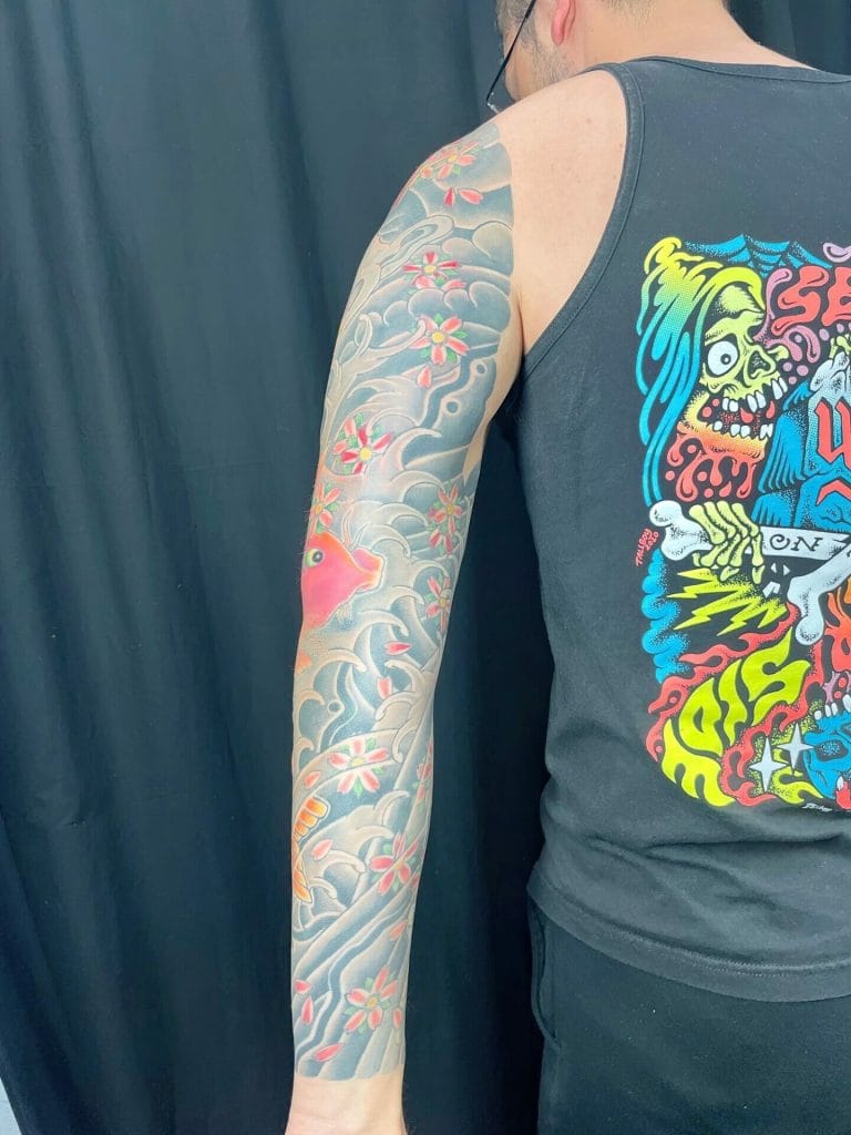 Colorful Japanese-style sleeve tattoo with flowers, clouds, and a fish on persons arm.