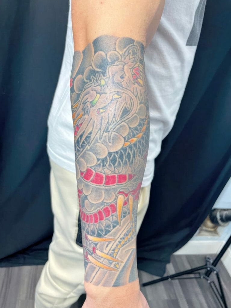 Colorful dragon tattoo with a fierce face, red tongue, and yellow claws on forearm.