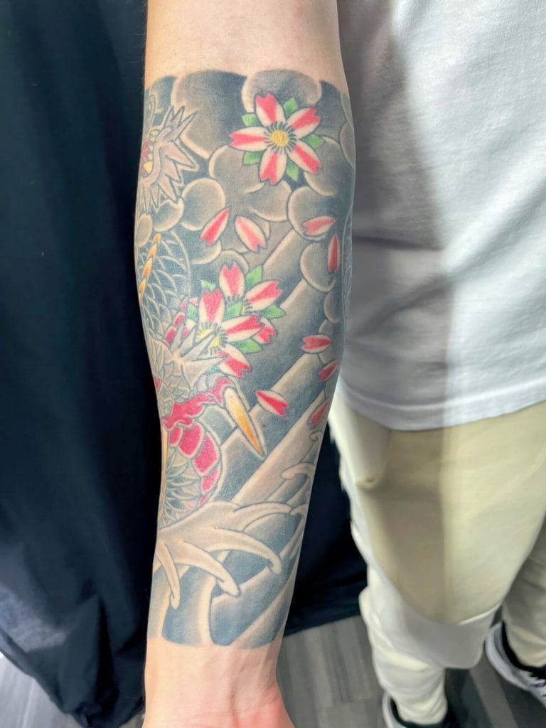 Colorful tattoo of cherry blossoms and a dragon on a persons forearm.