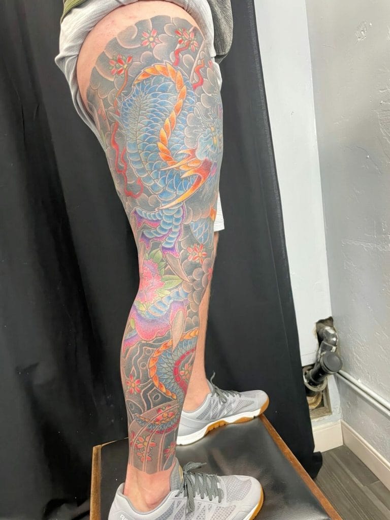 Colorful dragon tattoo covering the persons leg from thigh to ankle, with flowers and clouds.