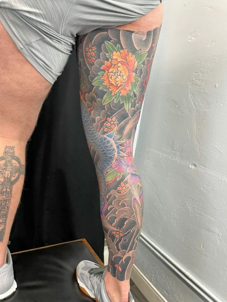 Colorful dragon and floral tattoo covering the persons leg from thigh to ankle.