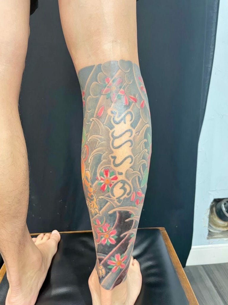 Colorful tattoo of a snake, cherry blossoms, and clouds on a persons lower leg.