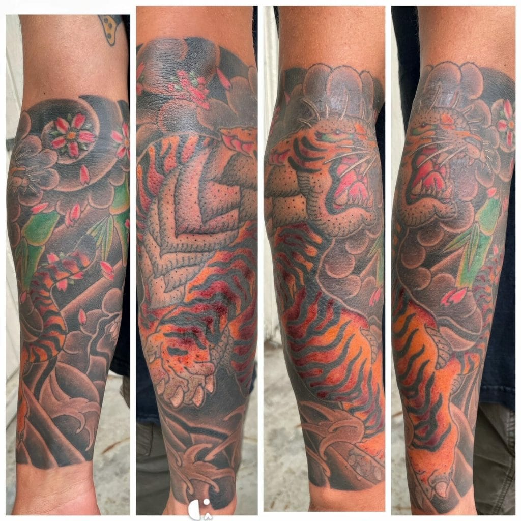 Tattoo of a roaring tiger with orange and black stripes, surrounded by pink flowers and green leaves.