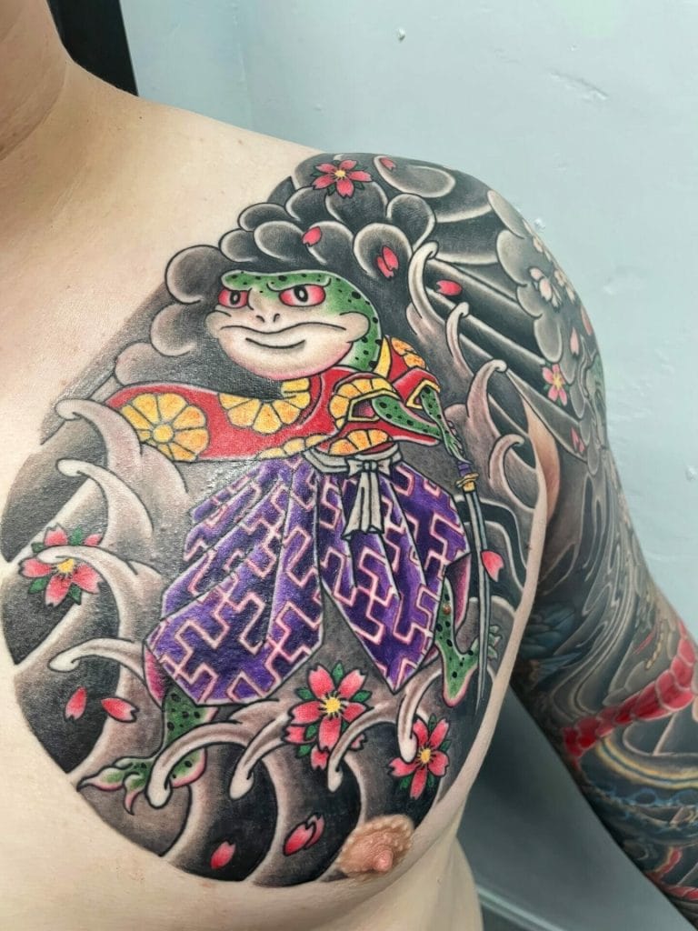 Colorful tattoo of a frog wearing traditional Japanese clothing surrounded by cherry blossoms.