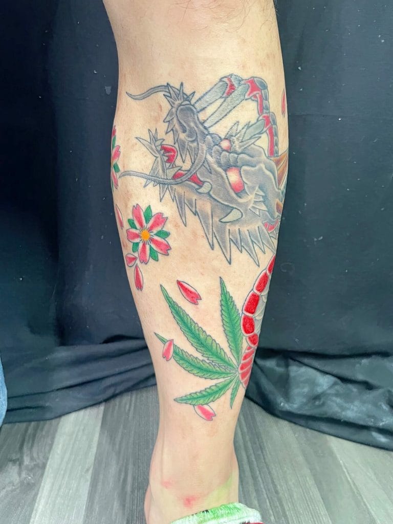 Dragon with red accents, pink flowers, and a large green cannabis leaf on the calf.