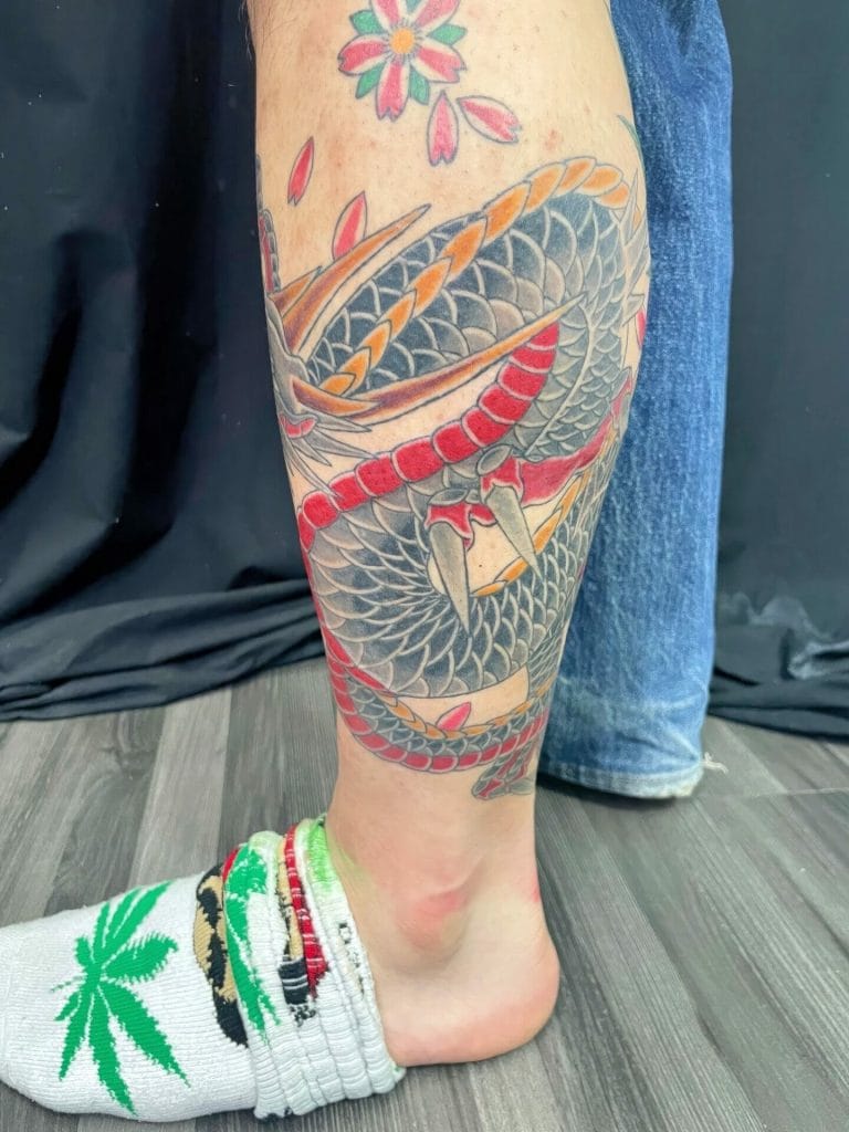Colorful snake tattoo wrapping around the lower leg, with a flower tattoo above.