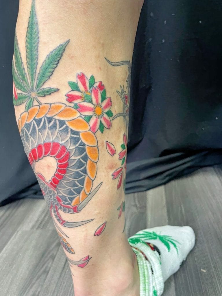 Colorful tattoo of a snake coiled among pink and green flowers on a persons leg.