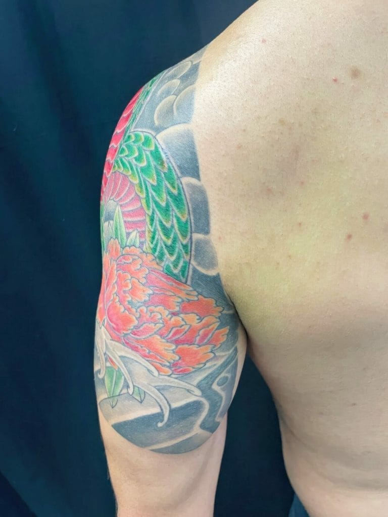 Colorful dragon tattoo covering the upper arm and shoulder with green, pink, and gray scales.