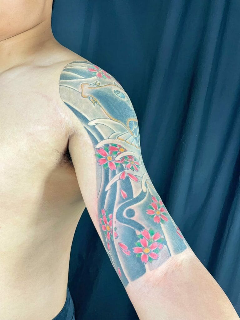 Colorful Japanese-style tattoo of cherry blossoms and a koi fish on persons upper arm.