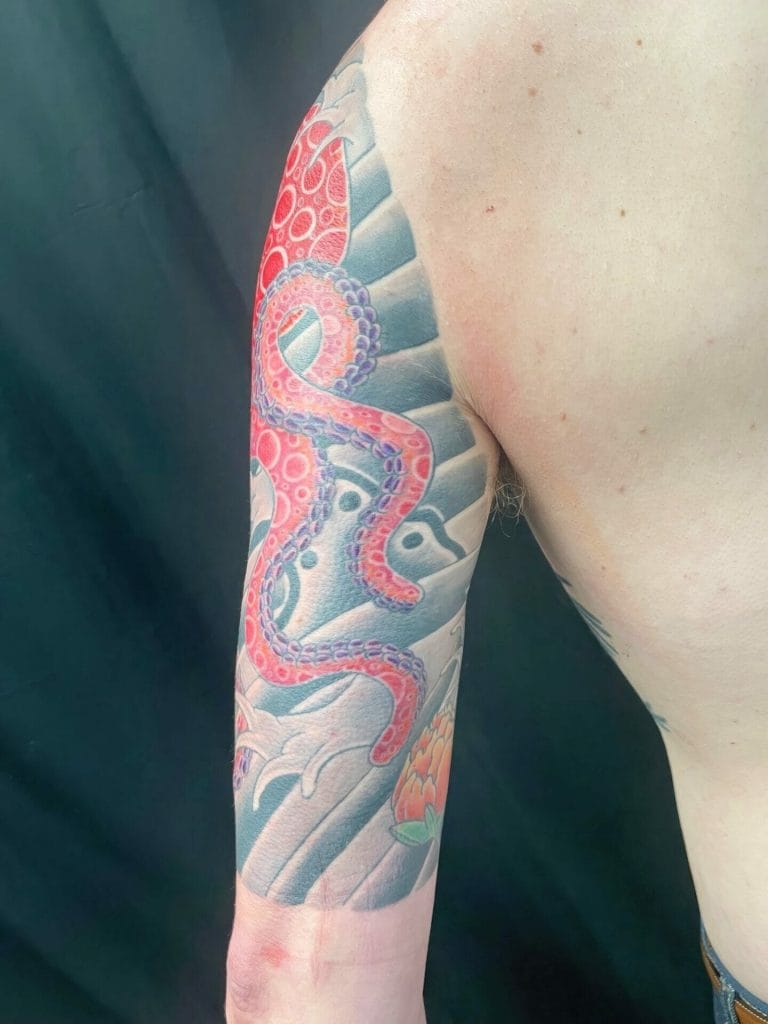 Colorful octopus tattoo on persons upper arm with waves and a peach flower in the background.
