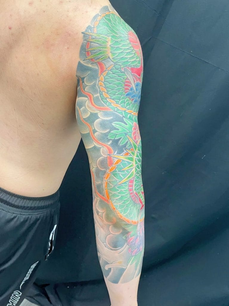 Colorful dragon tattoo covering the upper arm and shoulder with clouds and foliage.