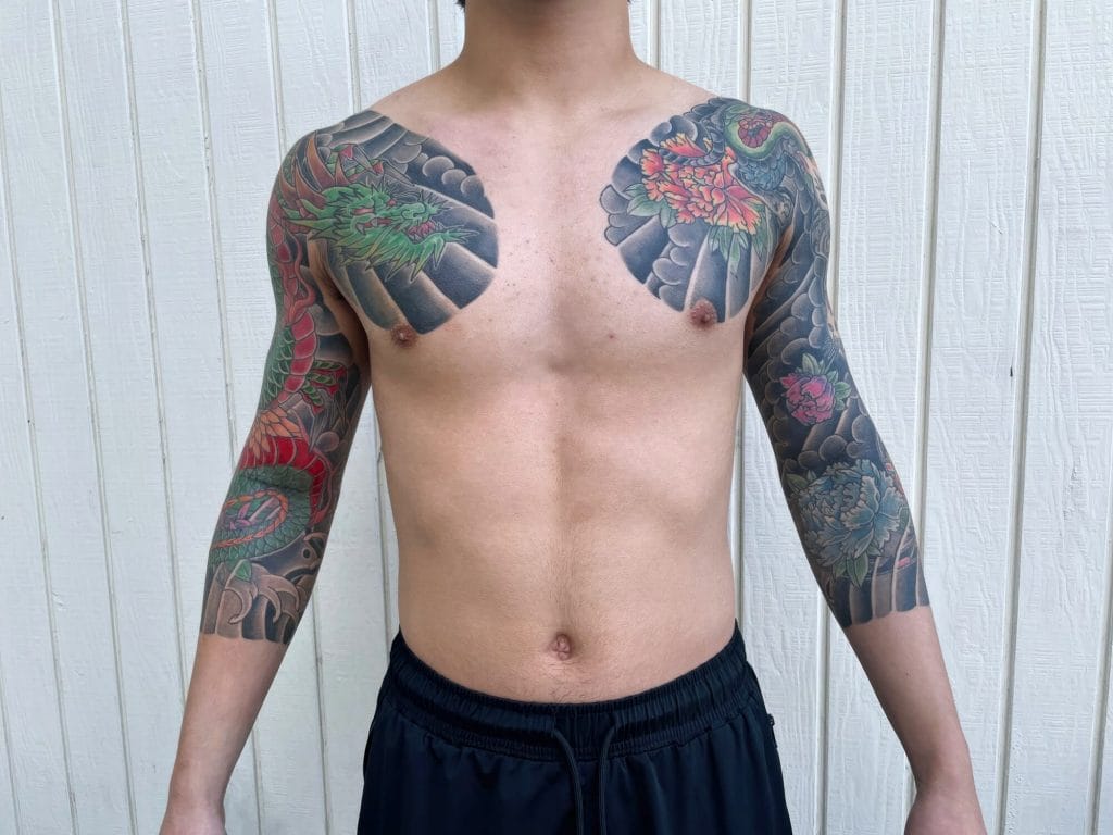 Man with colorful Japanese-style dragon and floral tattoos on shoulders and arms.