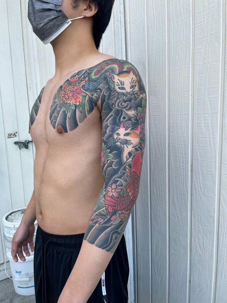 Colorful Japanese-style tattoo of cats, a snake, flowers, and a koi fish on the persons arm.