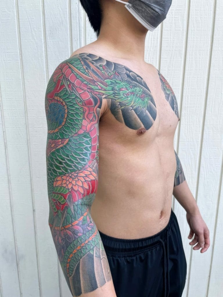 Colorful dragon tattoo covering the shoulder, upper arm, and chest of a shirtless person.