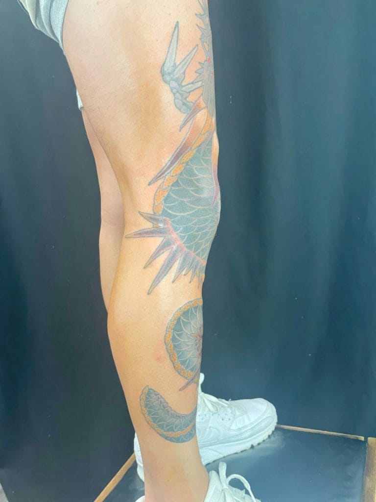 Colorful dragon tattoo wrapping around the persons calf and lower leg, with a dark background.