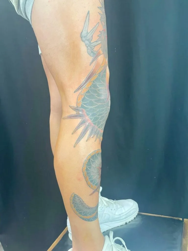 Colorful dragon tattoo wrapping around the persons calf and lower leg, with a dark background.