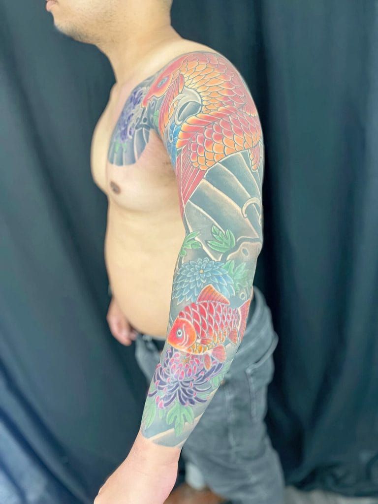 Colorful koi fish and floral tattoo covering the persons upper arm and shoulder.
