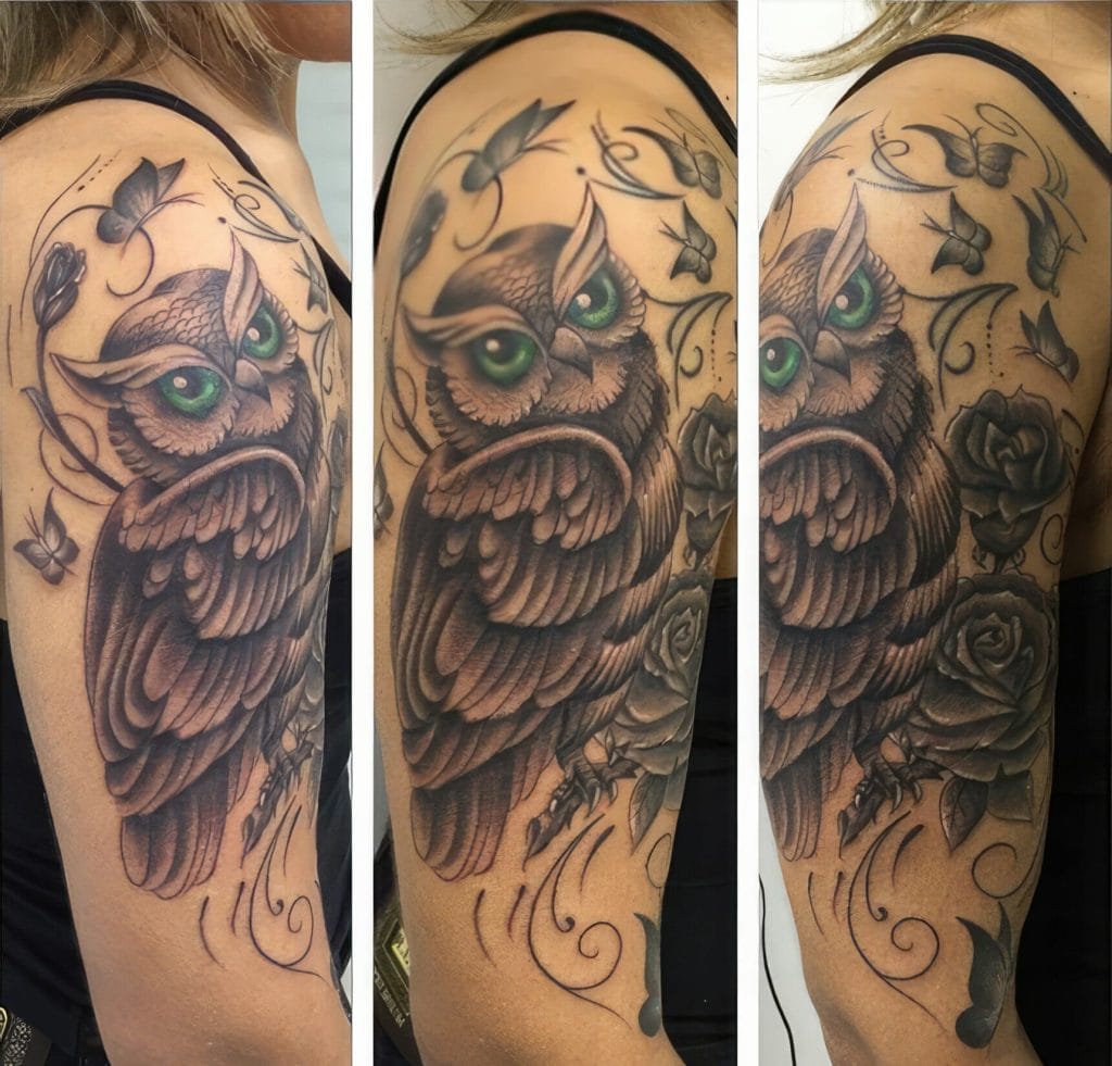 Tattoo of an owl with green eyes, surrounded by butterflies and roses on upper arm.