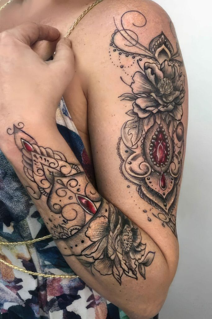 Detailed black and gray floral tattoo with red gemstone accents on upper arm and shoulder.