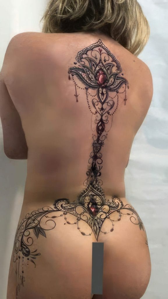 Intricate black and red floral tattoo running down the center of a persons back and hips.