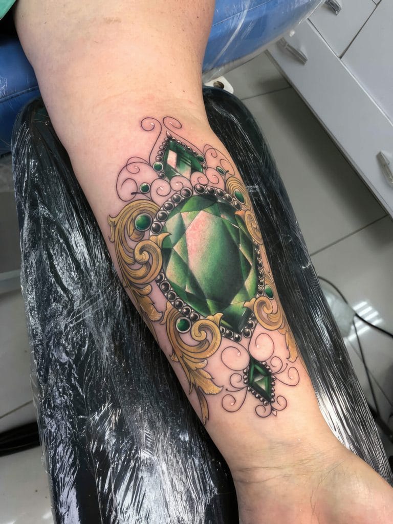 Detailed green gemstone surrounded by gold and black ornate swirls on persons leg.