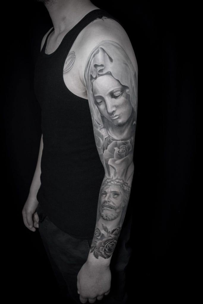 Black and gray tattoo of a womans face and a bearded mans face on a persons arm.